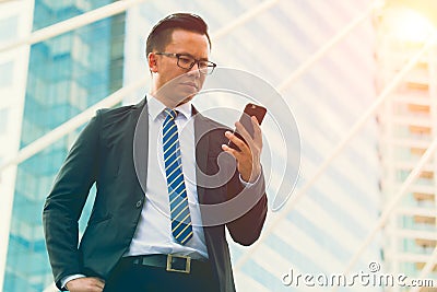 Modern young businessman wear black suit hand holding smartphone. Professional business man standing outside office Stock Photo