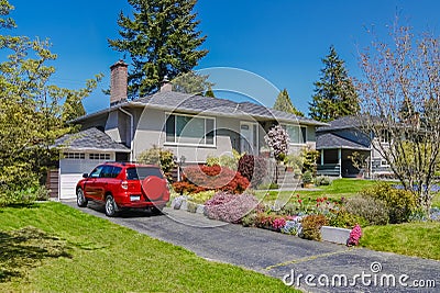 Modest residential house with red car parked on driveway in front. Family house with blossoming flowers on the yard Stock Photo