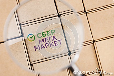 Modified photo of SberMegaMarket logo on a box under a magnifying glass surrounded by parcels Editorial Stock Photo