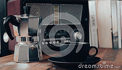Moka pot, vintage radio, a black coffee cup and saucer on a brown wooden table, with books Stock Photo