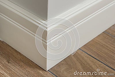 Molding in the interior, baseboard corner. Light matte wall with tiles immitating hardwood flooring Stock Photo