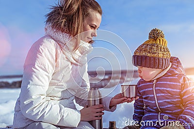 Mom with a boy son 3 years old, in the winter in a pair in the fresh air. Rest at the weekend resort, on the bench, a Stock Photo