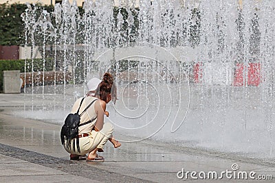 Mom and the child near the refreshing splashes of the summer city fountain. Bathing and rest in your free time in the rays of the Editorial Stock Photo