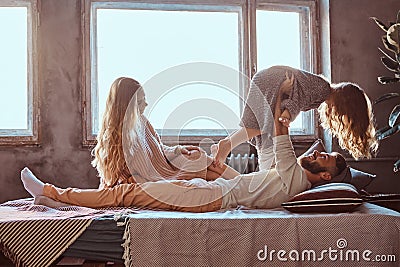 Mom, dad and daughter in bed. Father playing with adorable daughter in bedroom. Stock Photo