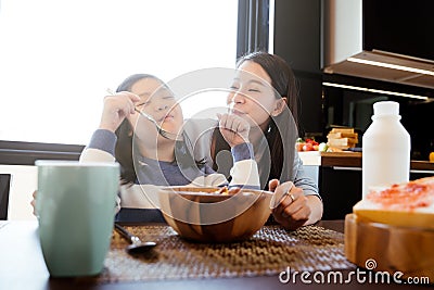 Mom and daughter eating Cereals with milk having breakfast in kitchen. Stock Photo