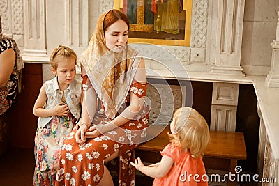 Mom with daughters sit on bench in Church Orthodox Stock Photo