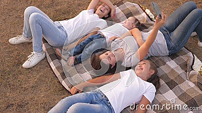 Mom and happy children are photographed on smartphone in park. Mother and daughters take a selfie while traveling, lying Stock Photo