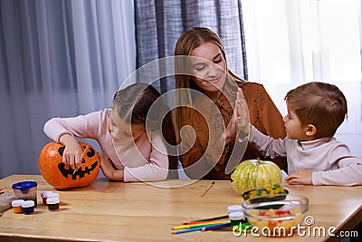 Mom and her kids are getting ready for Halloween. The girl paints a scary face on the pumpkin, while her mother slaps Stock Photo