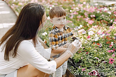 Mom helps her little son plant flowers in the pot in the greenhouse Stock Photo