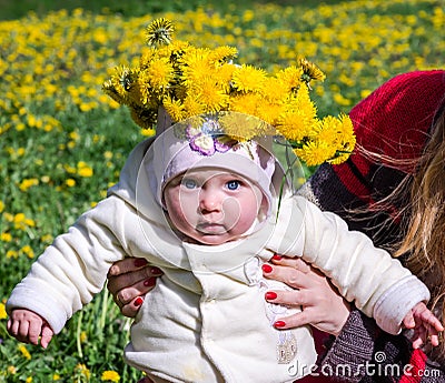 Mom holding the baby daughter a little girl with a bouquet of flowers of dandelions on the head that tries first steps Stock Photo