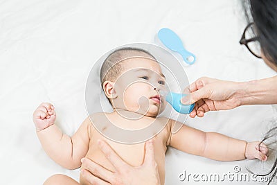 Mom holding her body to a small boy with her hands sucks the snot from the baby`s nose lying on the bed through the aspirator. Stock Photo