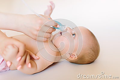 Mom holding her head to a small girl with her hands sucks the snot from the baby`s nose lying on the bed through the Stock Photo