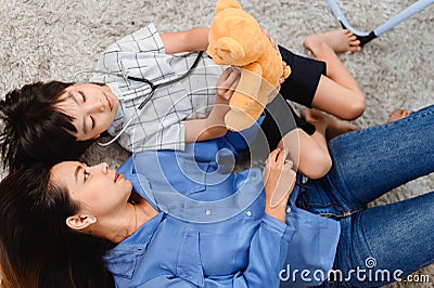 Mom and kid playing as doctor together in living room. Lifestyle and family activity. Asian mother with son Stock Photo