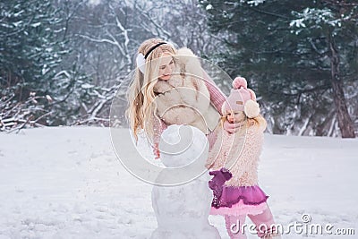 Mom and little daughter dressed in pink clothes have fun and make a snowman in a snowy park Stock Photo