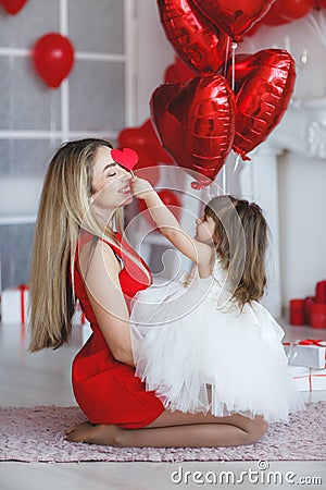 Valentine`s Day - young mother and little daughter in a room on the floor with gifts on a background of red heart-shaped balloons Stock Photo