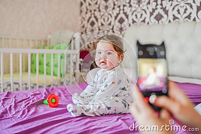 Mom photographs her baby on the phone. Mother takes a photo of her newborn baby on a smartphone. Family memories Stock Photo