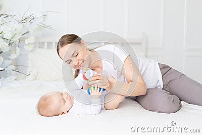 Mom plays with baby rattle on white bed at home Stock Photo