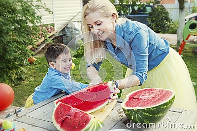 Mom and son cut a watermelon and laugh in the garden. Love and tenderness Stock Photo