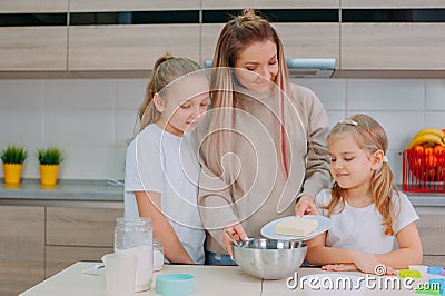 Mom teaches her daughters to cook dough in the kitchen Stock Photo