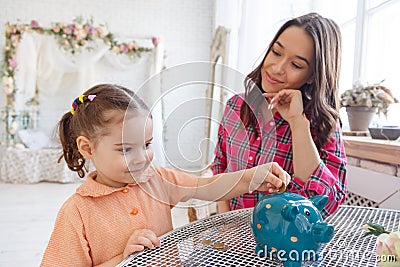 Mom teaches a little daughter to collect money in a piggy bank Stock Photo