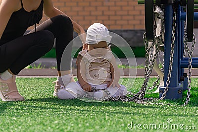 Mom and toddler daughter are walking on the sports ground near the house, the baby is interested in a exercise machine Stock Photo