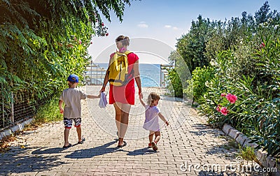Mom and two children hold hands and walk along the path to the sea on clear, sunny summer day on vacation Stock Photo