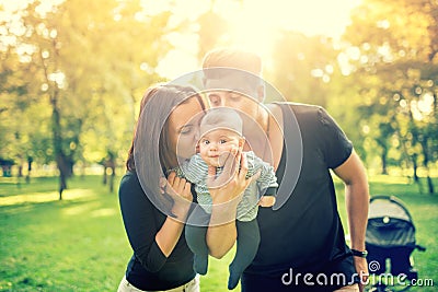 Mommy and daddy holding baby, 3 months old newborn and kissing him. Happy family with father, mother and infant. Vintage effect Stock Photo