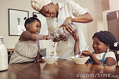 Mommy please add more. a young mother preparing cereal for her two adorable young daughters at home. Stock Photo