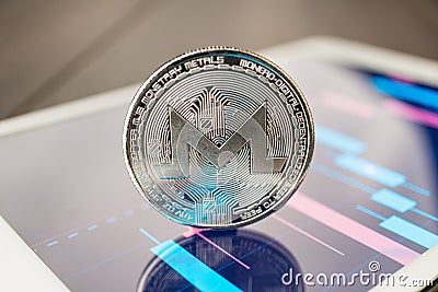 Close-up photo of monero cryptocurrency physical coin on the tablet computer showing stock market charts. trading monero crypto Editorial Stock Photo