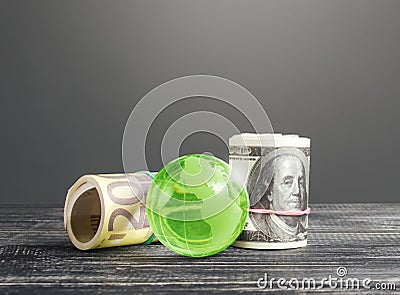 Money bundle rolls world currencies and a green glass globe. Capital investment, savings. Profit income, dividends payouts. Stock Photo