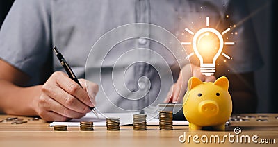 money and energy saving concept. businessman calculates savings on a table with a notebook and a piggy bank with light bulb icon. Stock Photo