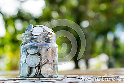 Money jar filled with coins on green bokeh Stock Photo