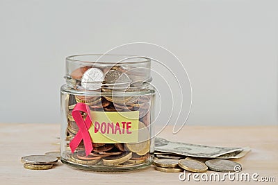 Money jar full of coins with pink ribbon and Donate label - Breast cancer charity and research fund concept Stock Photo