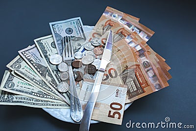 Money lying on the plate with fork and knife. Euros and dollars photo. Greedy corruption concept. Bribe idea. Cents coins. Stock Photo