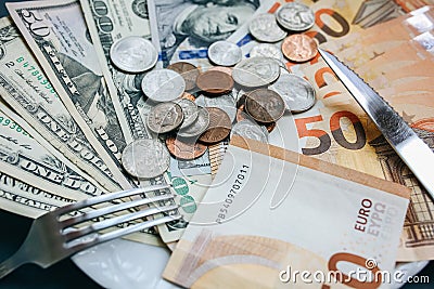 Money lying on the plate with fork and knife. Euros and dollars photo. Greedy corruption concept. Bribe idea. Cents coins. Stock Photo