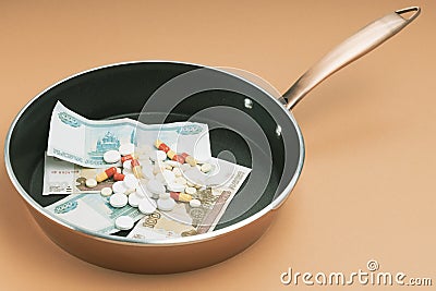 Money and pills in a frying pan, background orange Stock Photo