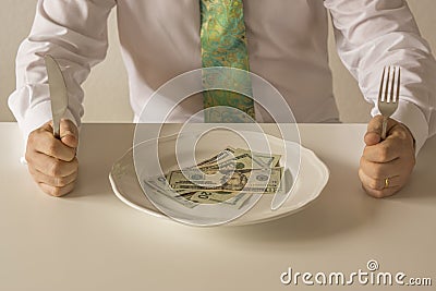 Money on a plate being cut like food with a knife and fork Stock Photo