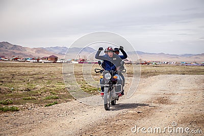 Mongolia Ulgii 2019-05-04 Mongolian men ride motorbike at steppe field on village background ang send greetings. Concept Editorial Stock Photo