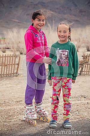 Mongolia Ulgii 2019-05-05 Two smiling Mongolian girls in colorful clothes on background of fence, mountains. Concept of Editorial Stock Photo