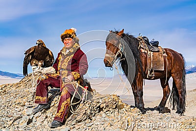 Mongolian Golden Eagle Hunter with his horse and a well trained golden eagle sat on the top of the mountain Editorial Stock Photo