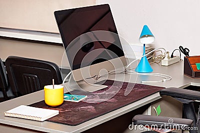 A monitor screen on a desktop along with a yellow cup and a turquoise table lamp Stock Photo