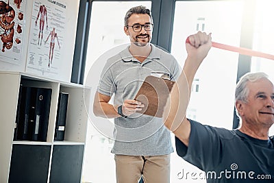 Monitoring his progress with a smile. a friendly physiotherapy supervising his mature patient while he works out in the Stock Photo