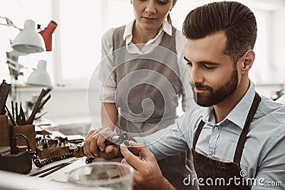 Monitoring of progress. Close-up portrait of young male jeweler polishing a ring while female master is observing the Stock Photo