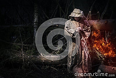 A monk in a cassock walks through the night forest with a sword and a lantern. Stock Photo