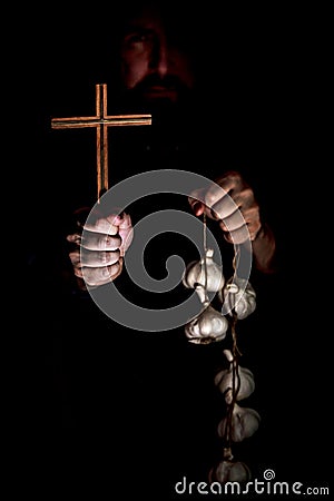 Monk in the dark holding a crucifix and a garlic string, vampire cult and their protection Stock Photo
