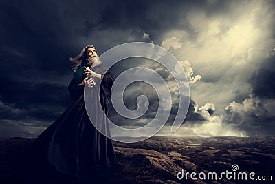 Monk Holding Bible Looking Up to God Sky Light, Old Priest in Black Robe in Storm Stock Photo