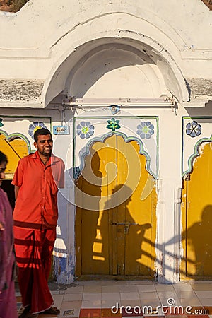 Monk in orange dress looking the camera in front of a yellow door of the temple Editorial Stock Photo