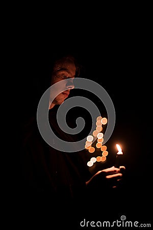 Monk portrait human face hold candle fire light and pray in darkness environment space vertical photography soft focus concept Stock Photo