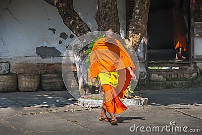 A Monk wearing his traditional orange/yellow robe is leaving a monastery in Luang Prabang, Laos Editorial Stock Photo