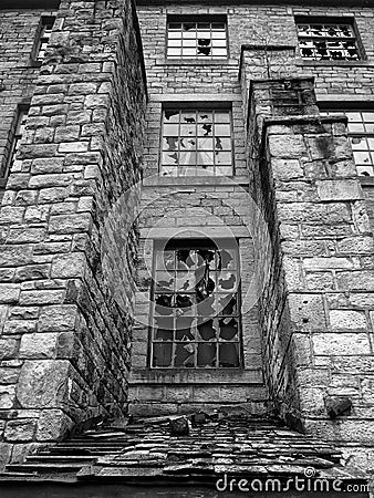 Monochrome image of broken windows in an empty abandoned vandalized old stone building Stock Photo